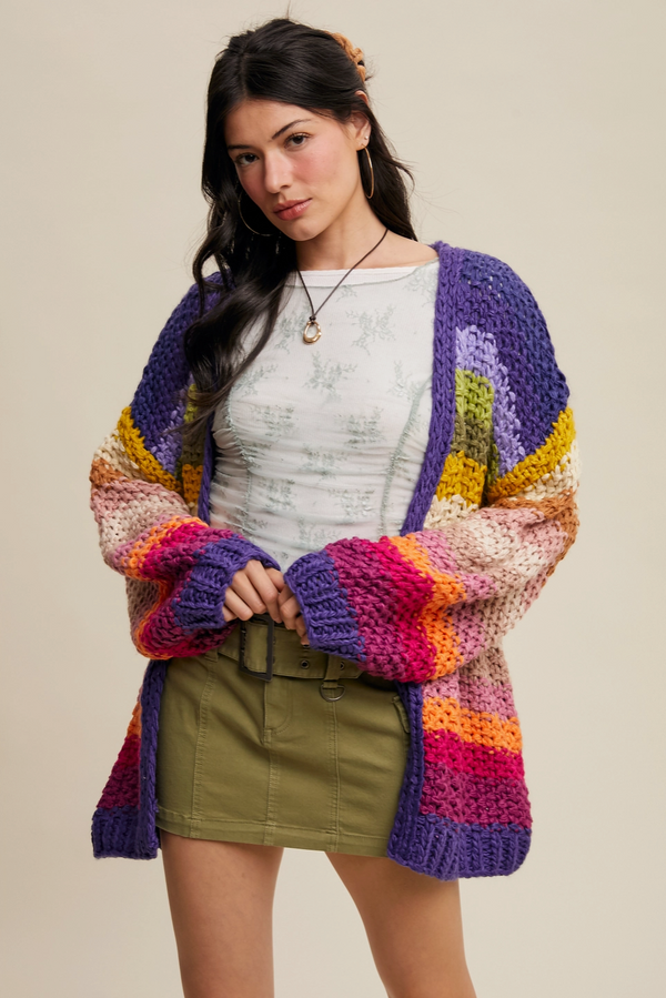 Woman wearing a colorful crocheted cardigan over a white shirt and green skirt on a beige background