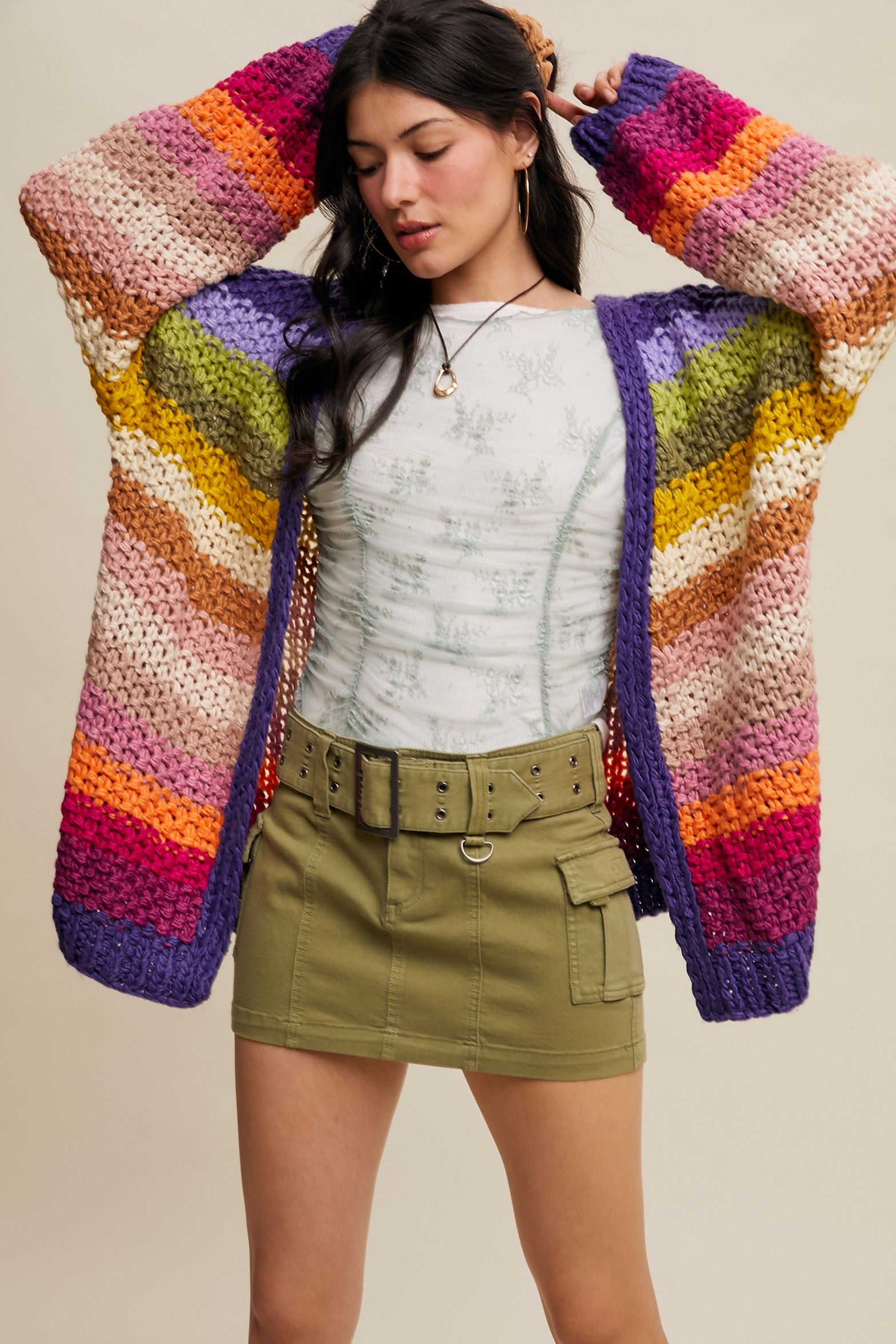 Woman wearing a colorful striped cardigan over a white top and green skirt.