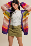 Woman wearing a colorful striped cardigan over a white top and green skirt.