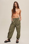 Woman wearing a peach tank top and olive green cargo pants on a beige background