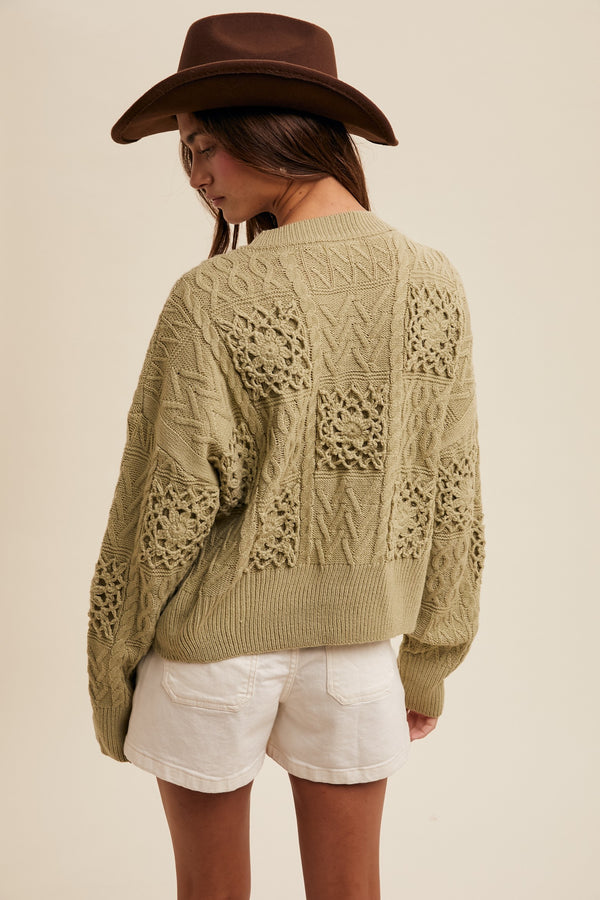 Person wearing a green knitted cardigan with lace details, white shorts, and a brown hat on a beige background.