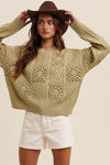 Woman wearing a patterned beige sweater and white shorts with a brown hat on a plain background