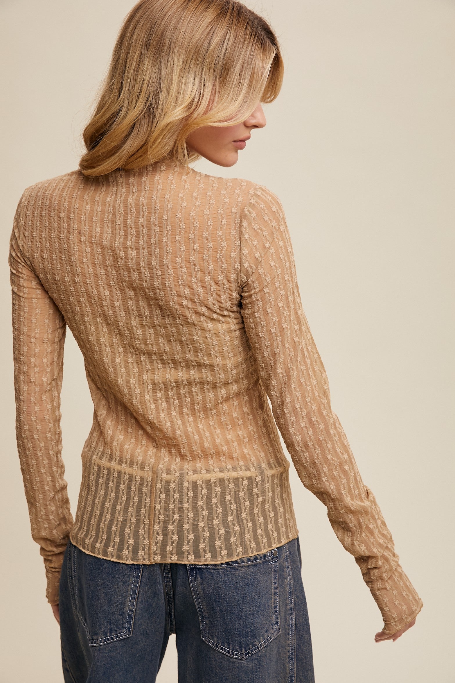 Woman wearing a brown ribbed sweater and blue jeans against a beige background