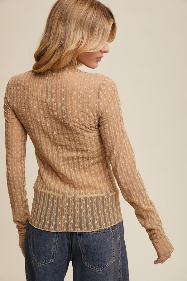 Woman wearing a brown ribbed sweater and blue jeans against a beige background