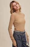Woman wearing a ribbed brown sweater and dark jeans against a beige background