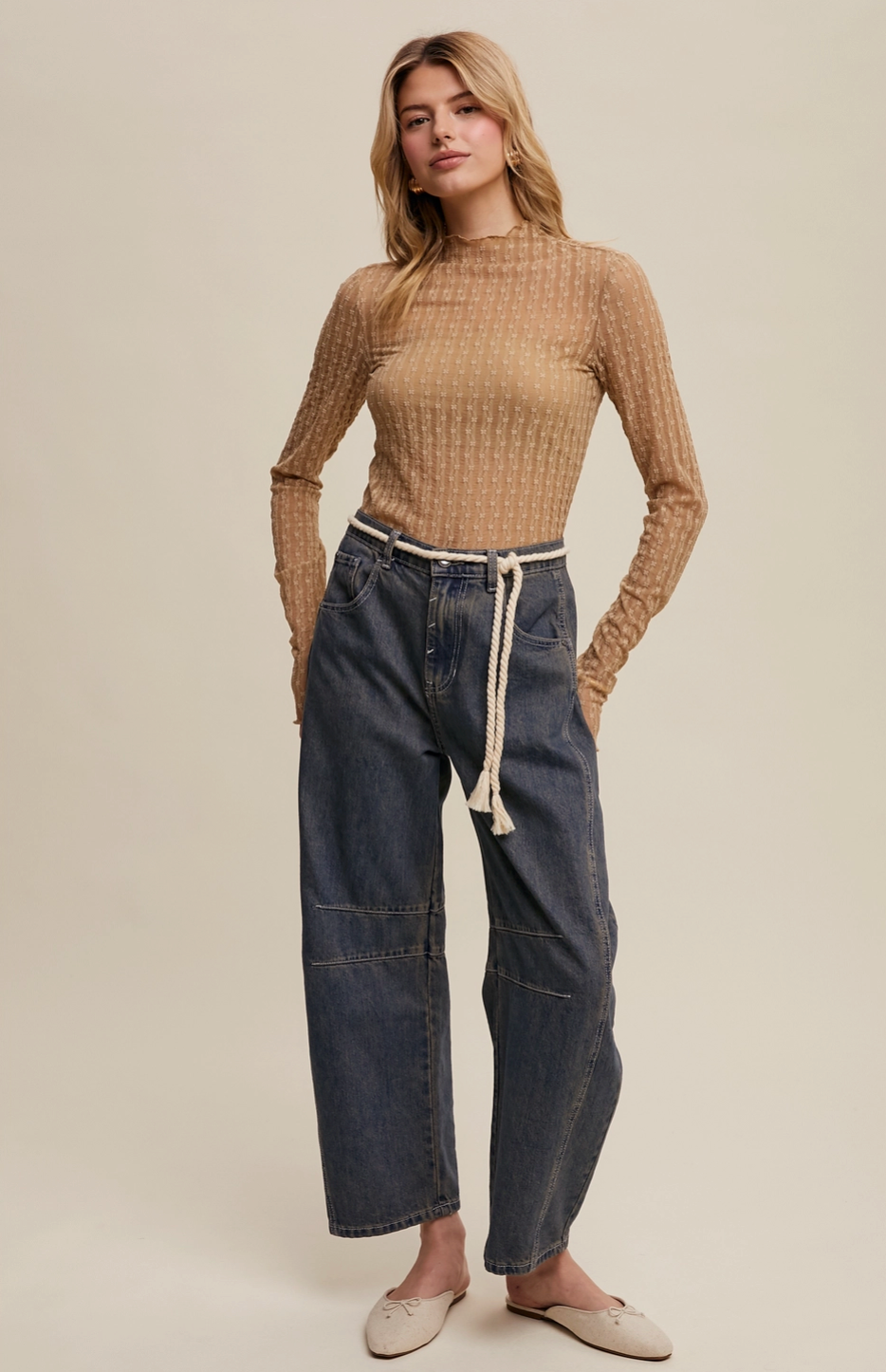 Woman wearing a ribbed sweater and wide-leg jeans on a plain background
