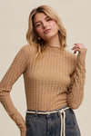 Woman wearing a brown textured top and blue jeans against a beige background