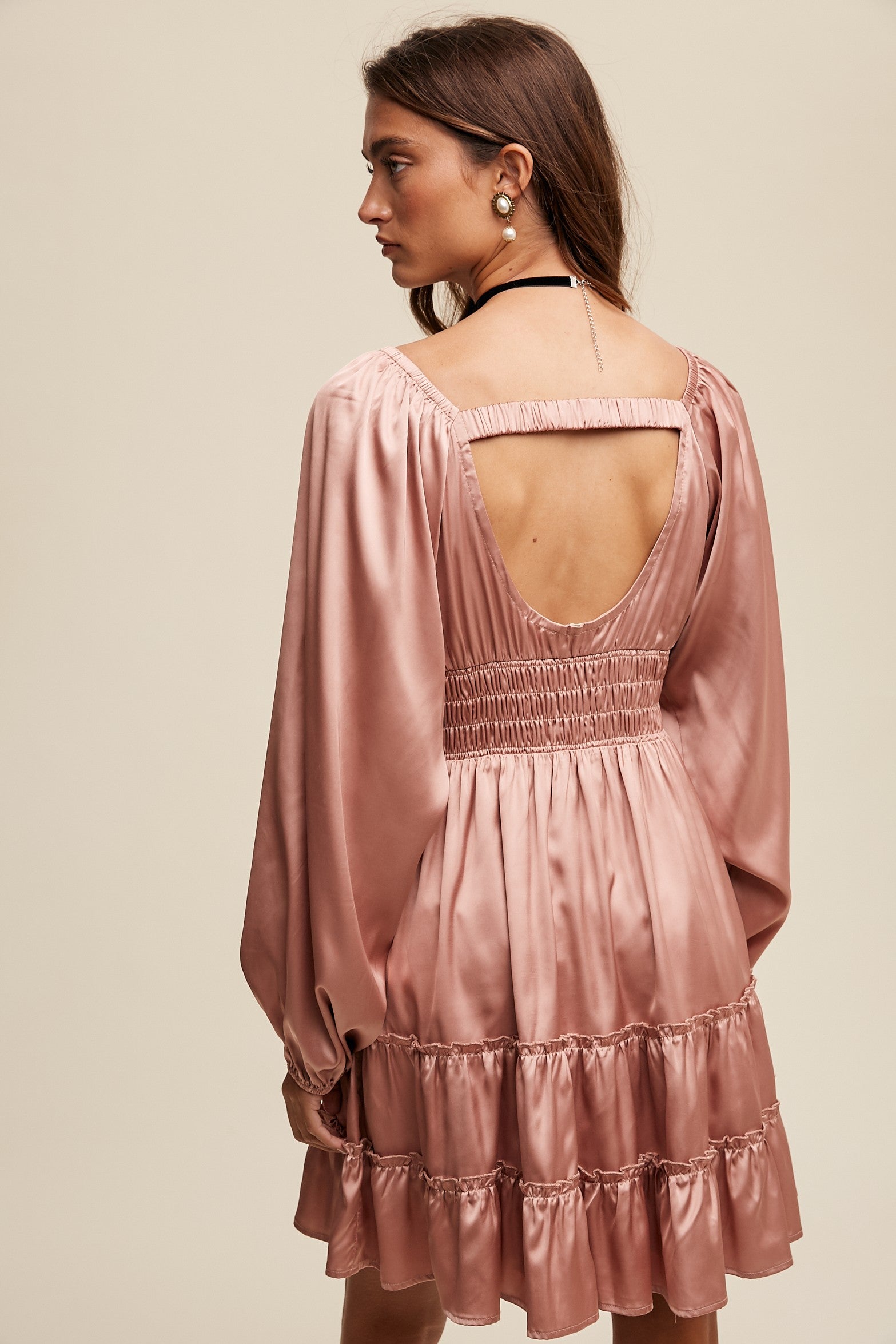Woman wearing a pink dress with long sleeves and an open back on a beige background