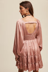 Woman wearing a pink dress with long sleeves and an open back on a beige background