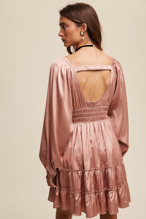 Woman wearing a pink dress with long sleeves and an open back on a beige background