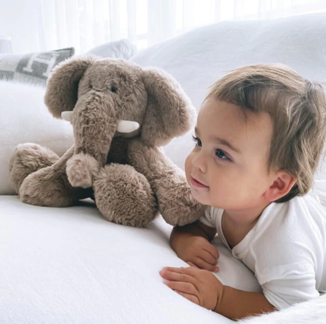 Child lying on a bed with a plush elephant toy