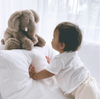 Child interacting with a large plush elephant toy on a bed.