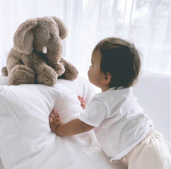 Child interacting with a large plush elephant toy on a bed.
