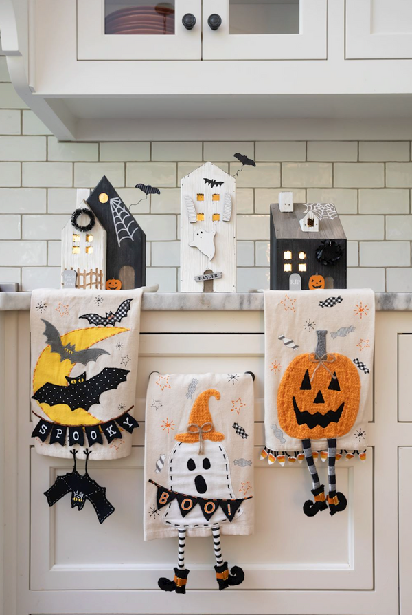 Set of Halloween-themed kitchen towels with ghost, bat, and pumpkin designs on a kitchen counter.
