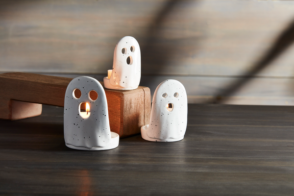 Three ceramic ghost-shaped candle holders on a wooden surface with a neutral background