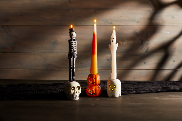 Halloween-themed candles with skeleton, ghost, and jack-o'-lantern designs against a wooden background.