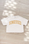 White t-shirt with 'SUNKISSED' text on a wooden floor