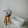 Gray caddy with baby items on a wooden stool next to a white bathtub in a bathroom.
