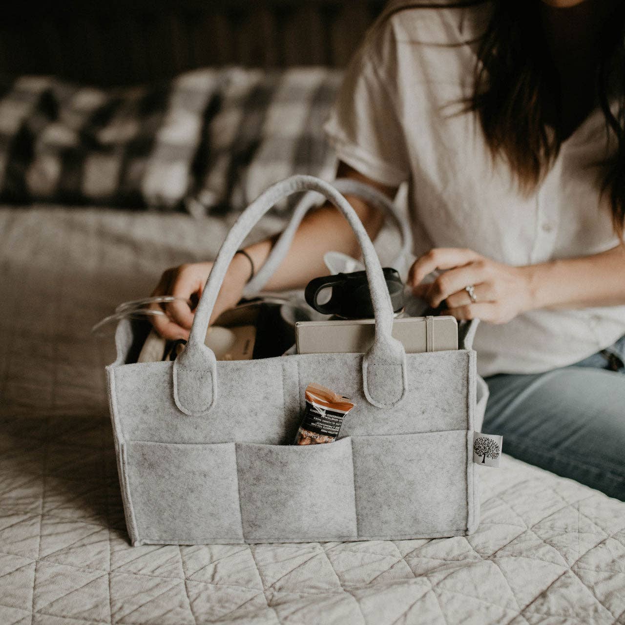 Person organizing items in a gray felt caddy on a bed.