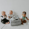 Three babies playing with a gray diaper bag on a white floor.