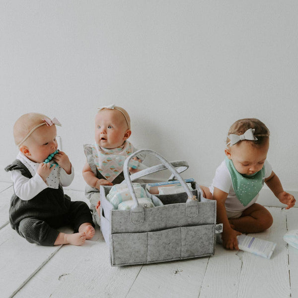 Three babies playing with a gray diaper bag on a white floor.