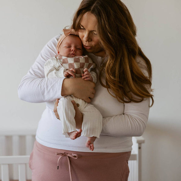 Woman holding a baby in a room with a crib in the background