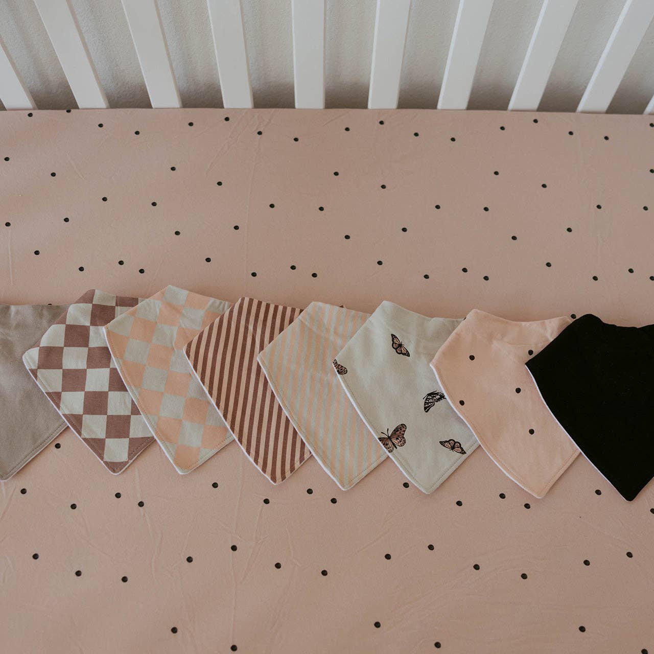 Collection of baby bibs on a pegboard with polka dot background