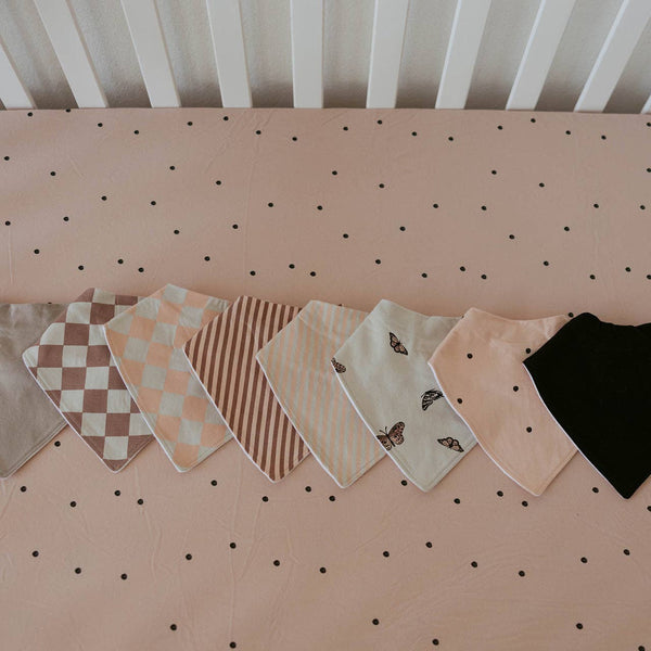 Collection of baby bibs on a pegboard with polka dot background