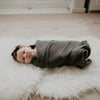 Baby wrapped in a gray blanket lying on a white fluffy rug