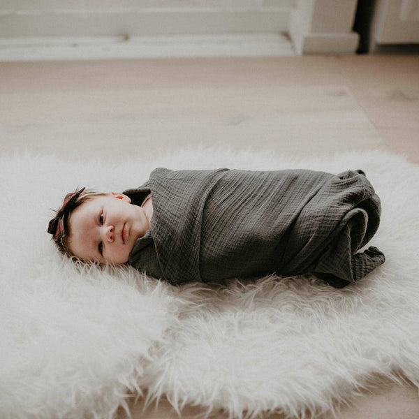 Baby wrapped in a gray blanket lying on a white fluffy rug