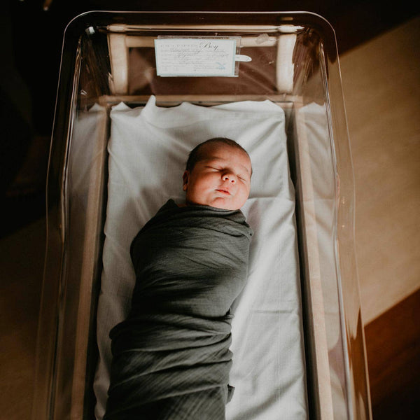 Newborn baby wrapped in a blanket lying in an open metal coffin.