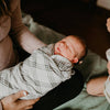 Newborn baby swaddled in a checkered blanket held by a person, with a blurred background