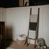 Wooden ladder with blankets against a white paneled wall in a room.