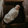 Baby swaddled in a blanket lying on a brown leather couch
