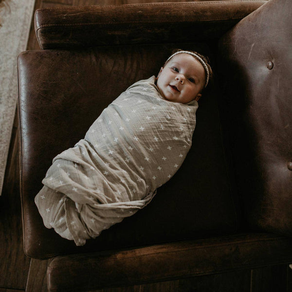 Baby swaddled in a blanket lying on a brown leather couch
