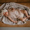 Newborn baby lying on a brown couch with a blanket, wearing a white headband.