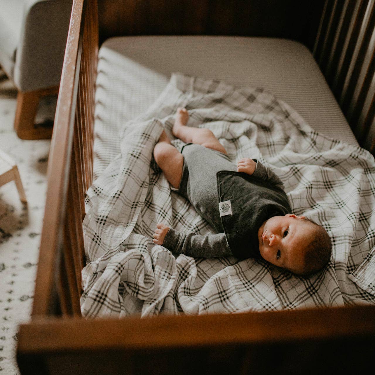 Baby lying on a plaid blanket in a crib