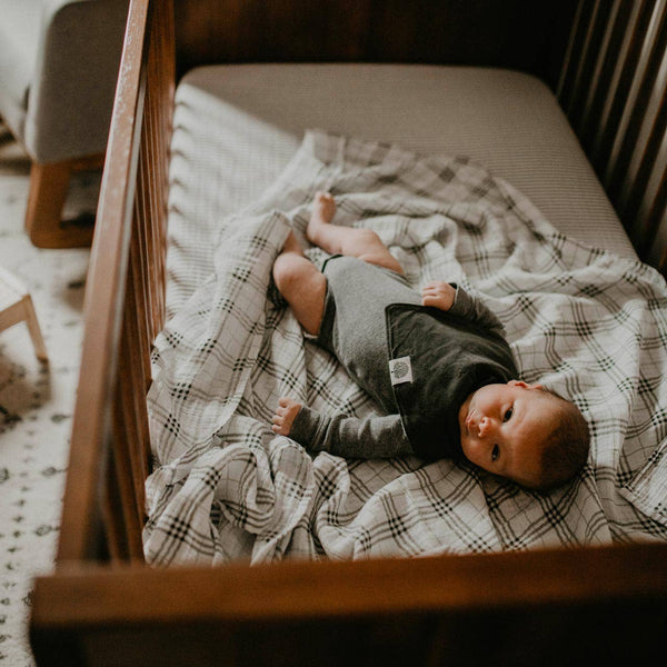 Baby lying on a plaid blanket in a crib