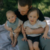 Man holding two young children outdoors on a checkered blanket