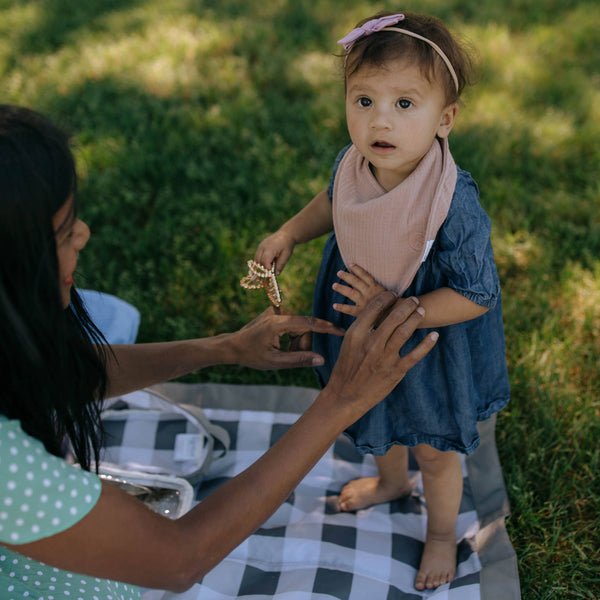 Woman interacting with a young child outdoors on a checkered blanket