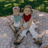 Two young children sitting on a patterned blanket outdoors.