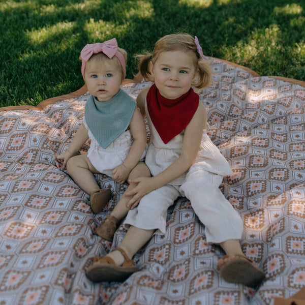 Two young children sitting on a patterned blanket outdoors.