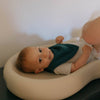 Baby lying on a white cushion with a green bib