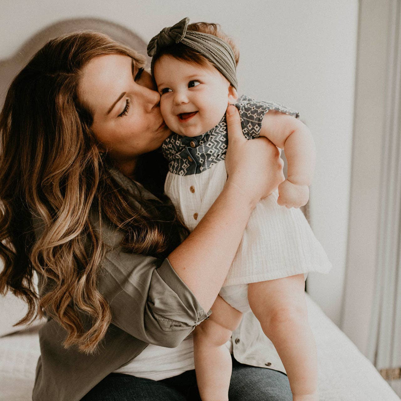 Woman kissing a baby on the cheek in a cozy indoor setting