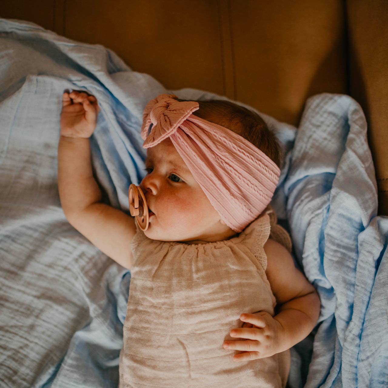 Baby wearing a pink headband lying on a textured blanket