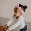 Child wearing a pink headband and white long-sleeve shirt with a blurred background