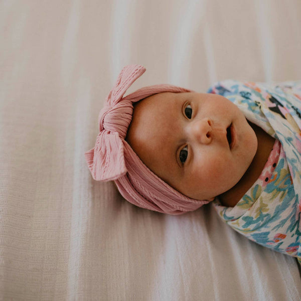 Baby wearing a pink headband and floral outfit on a beige blanket