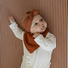 Baby wearing a rust-colored headband and bib against a striped background
