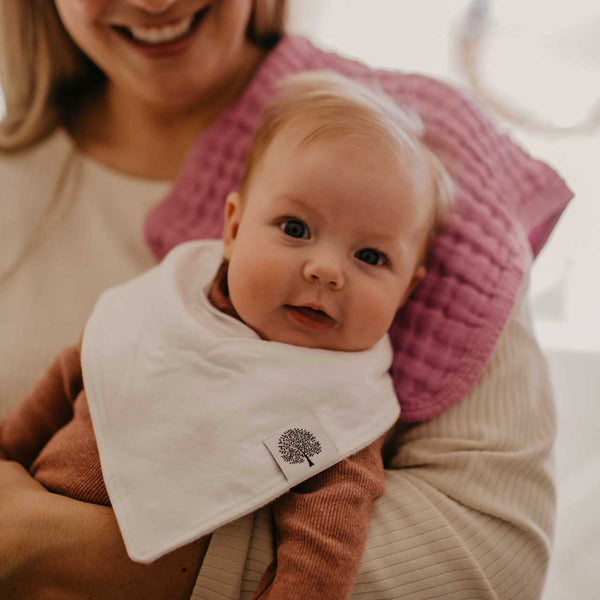 Baby wearing a white bib with a tree design, held by a smiling person.