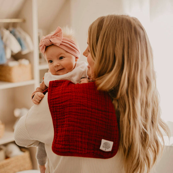 Woman holding a baby wrapped in a red blanket with a pink headband.